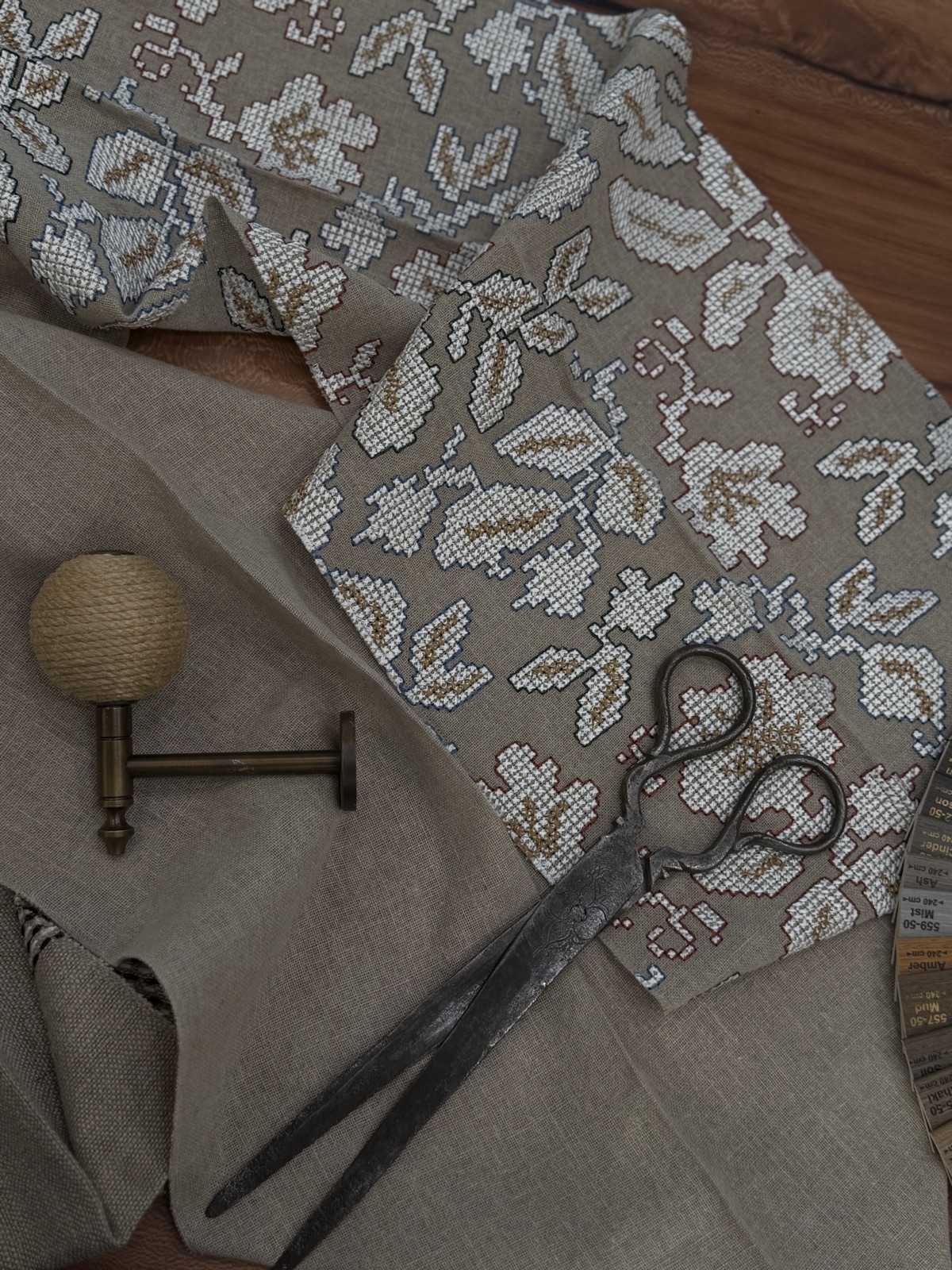 Tailoring scissors resting on a length of embroidered floral fabric with a brass curtain finial
