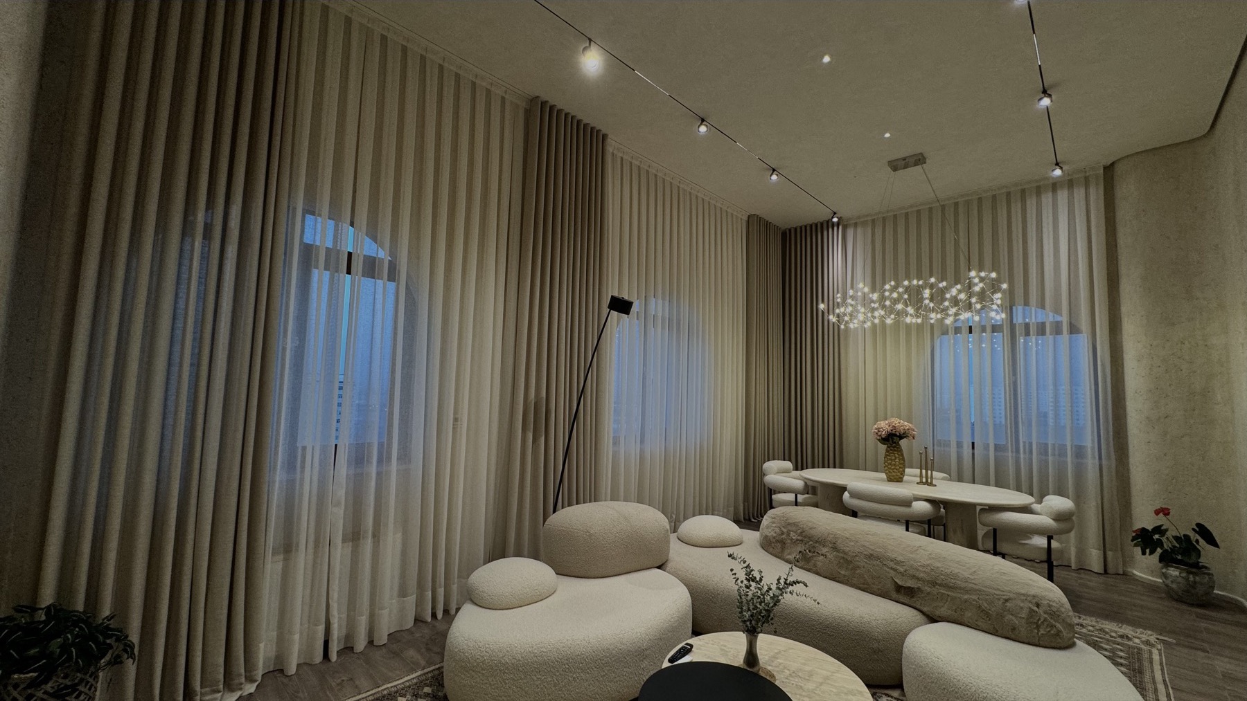 A reception room with floor-to-ceiling sheer curtains, an evening skyline visible through the window and a sculptural chandelier above the table