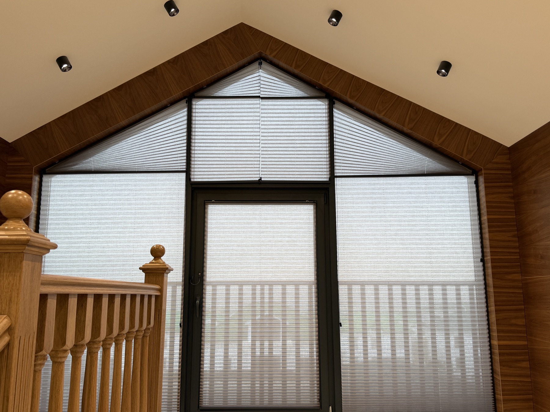 Pleated cellular shades fitted to a gable peaked window in a wood-panelled stairwell