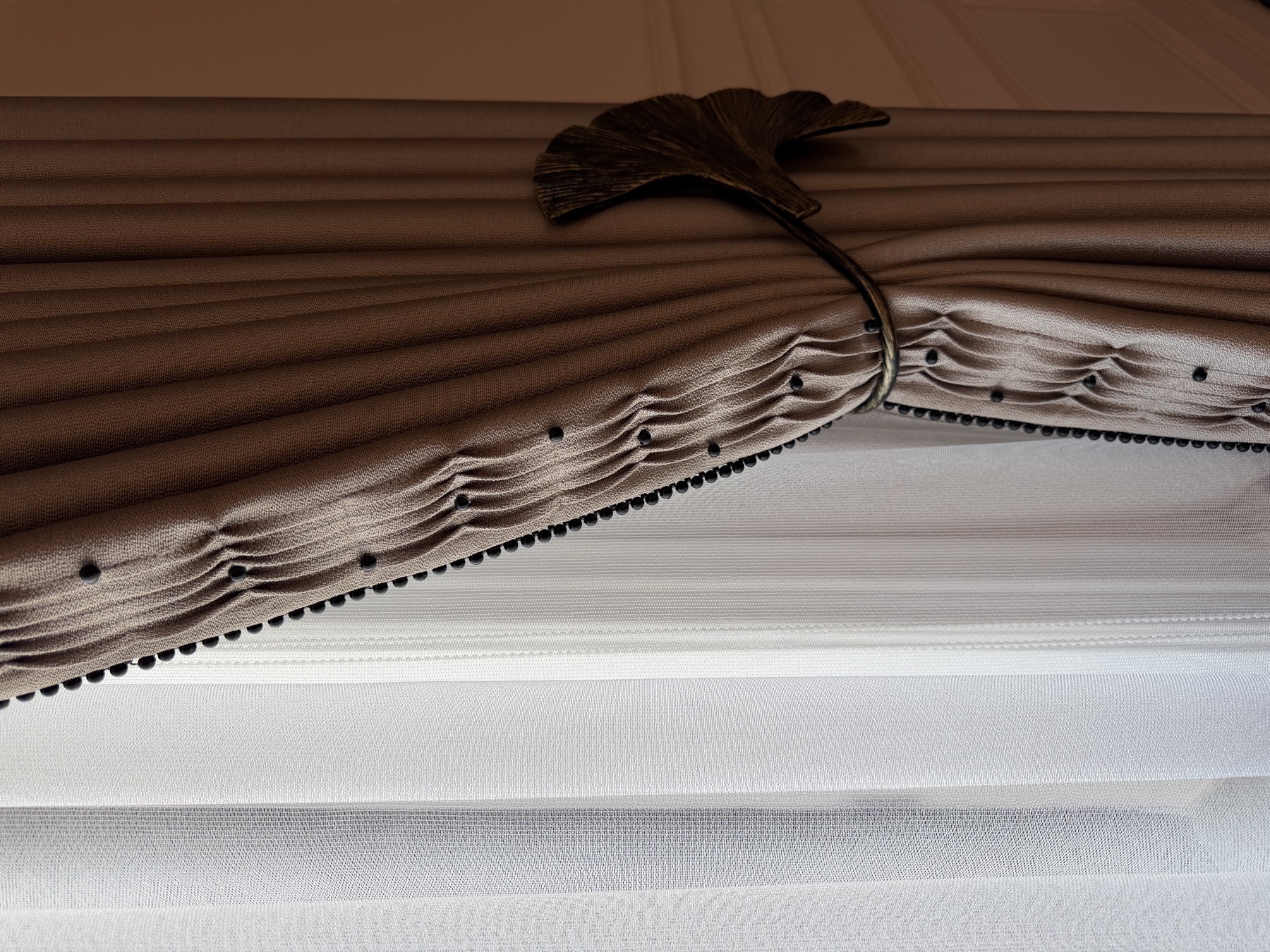 Bronze ginkgo leaf bracket and beaded edge on a champagne-coloured curtain valance with sheers below