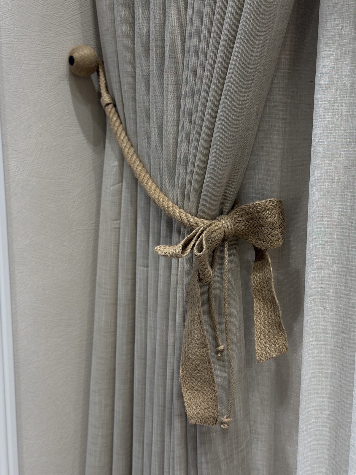 A jute rope tieback finished with a braided hessian bow gathering a pleated linen drape