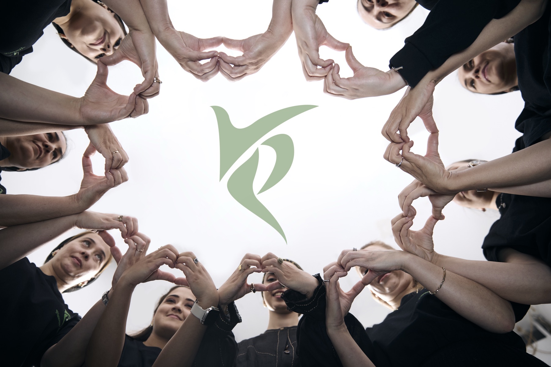 Hands of the team forming a circle of hearts around the Yasemin logo
